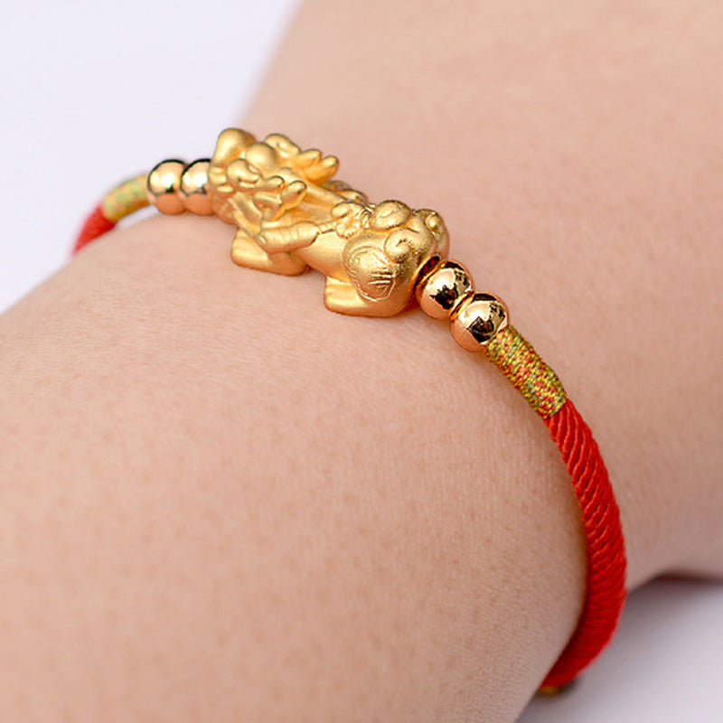 Gold bracelet with a dragon design on a red string worn on a wrist.