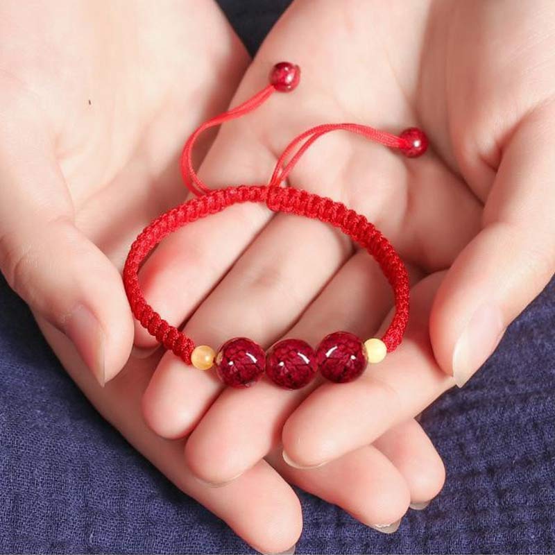 Red string bracelet with beads held in hands on a blue fabric background