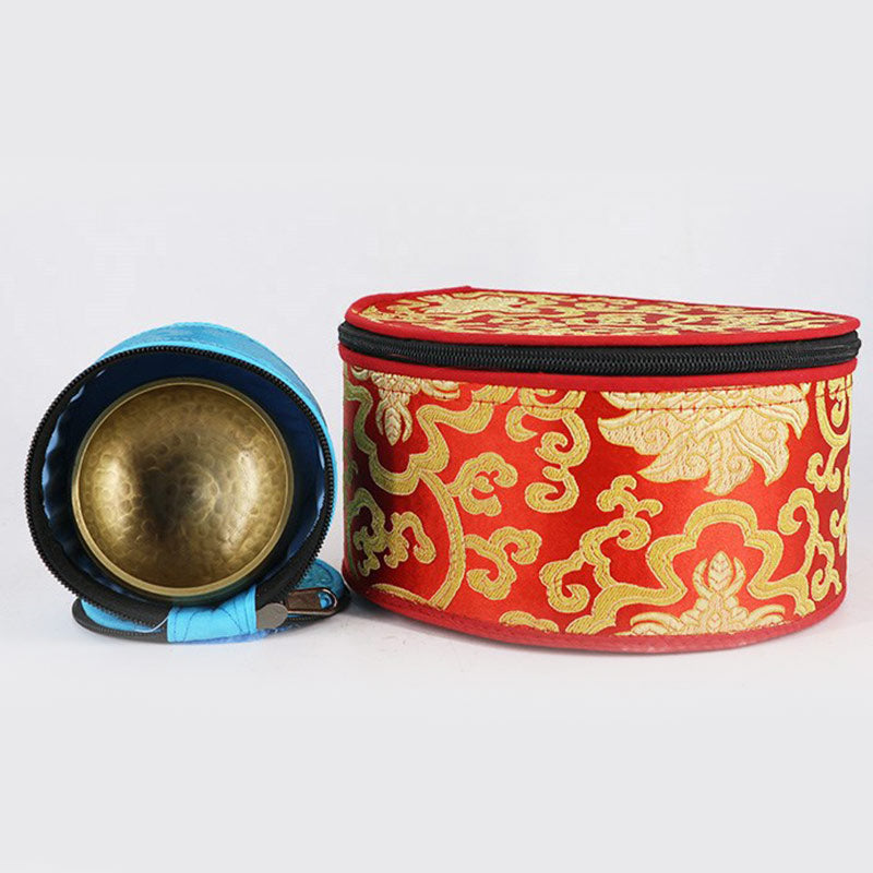 Brass singing bowl with a red and gold patterned case on a white background