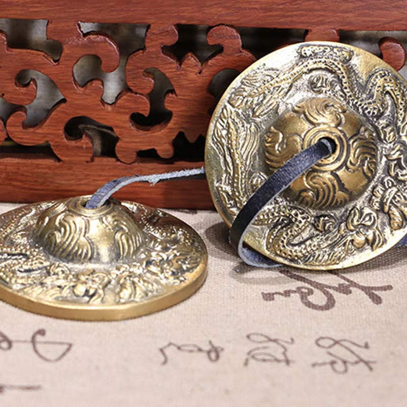 Two brass gongs with intricate designs on a wooden stand and textured surface.