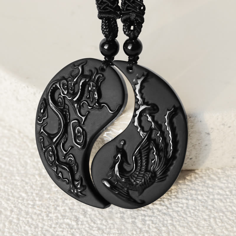 Black yin yang pendant with dragon and phoenix design on a white fabric background