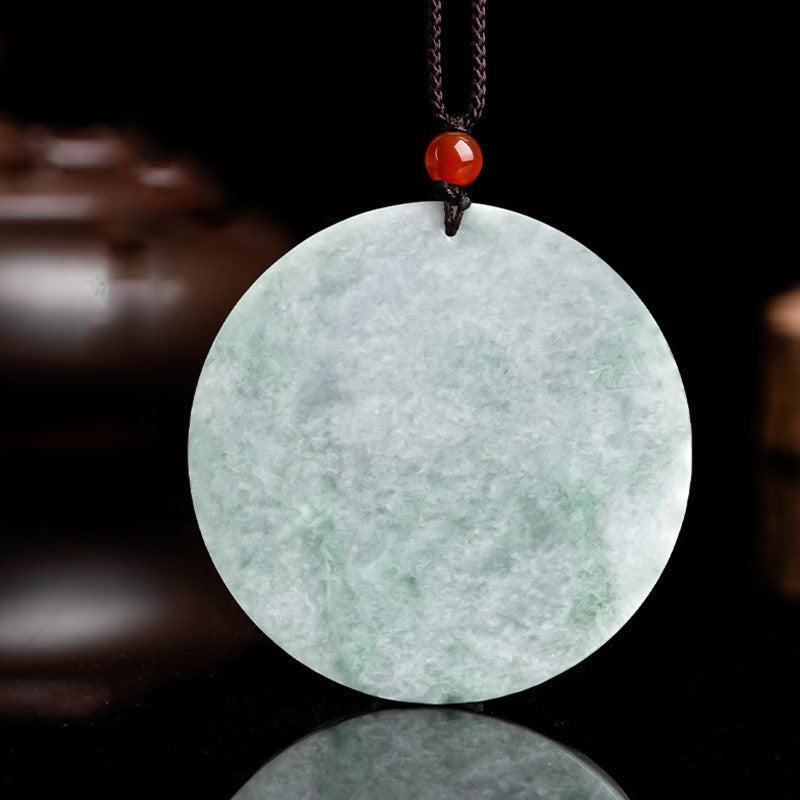 Green jade pendant with a red bead on a dark background