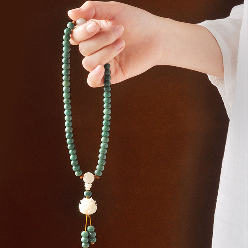Hand holding a green beaded necklace with a white pendant against a dark background