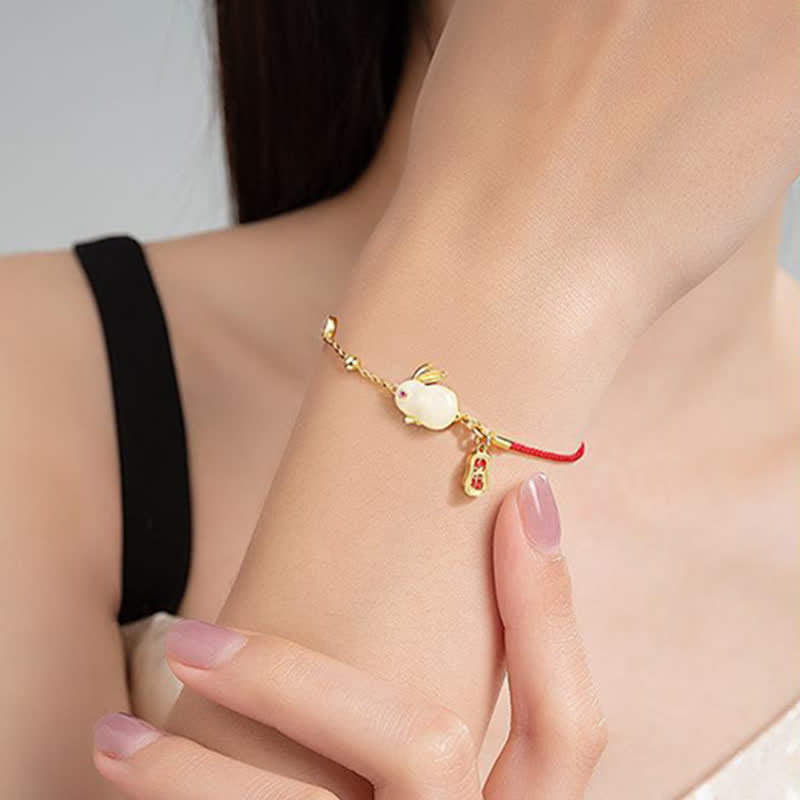 Gold bracelet with a red charm on a person's wrist against a neutral background