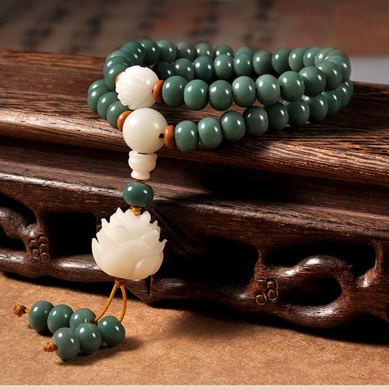 Green beaded bracelet with white lotus flower charm on a wooden surface