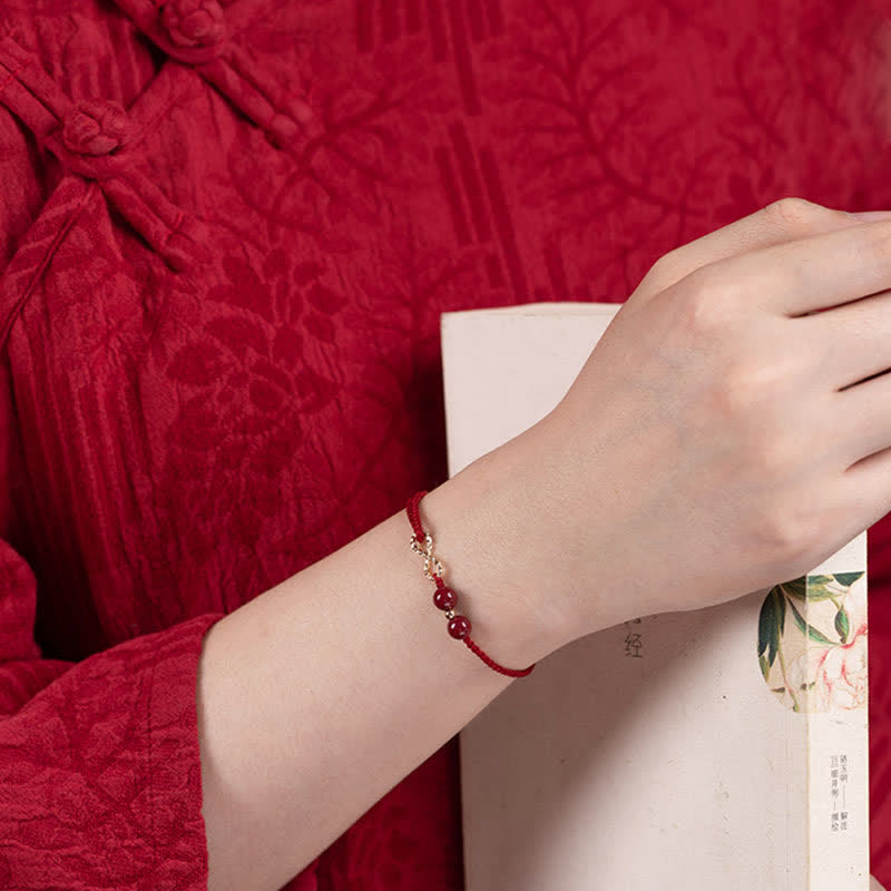 Hand wearing a red beaded bracelet against a red textured fabric background