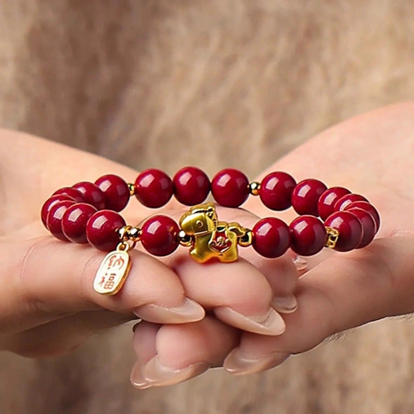 Red beaded bracelet with gold charm held between fingers against a blurred background