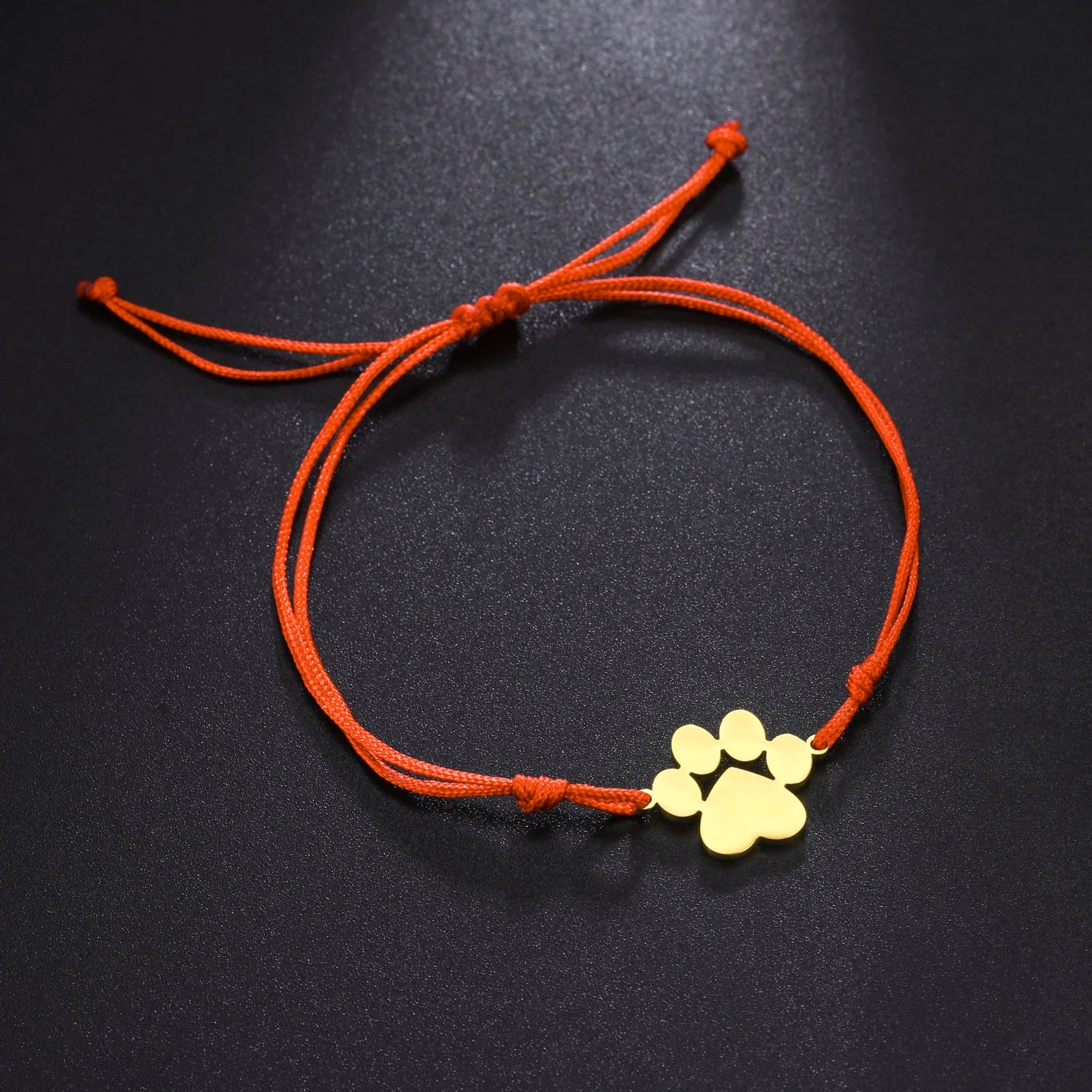 Bracelet with gold paw print charm on an orange cord against a black background