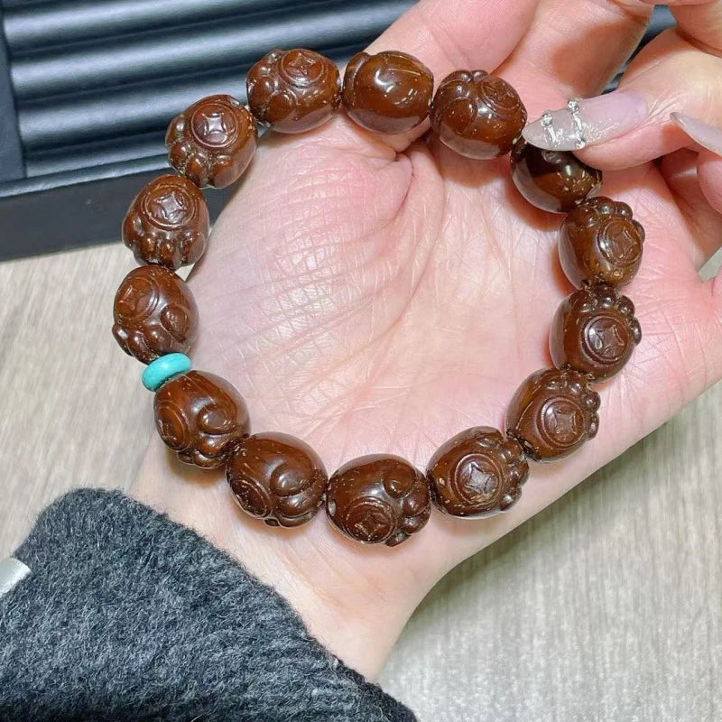 Brown beaded bracelet with a turquoise charm held in a hand.