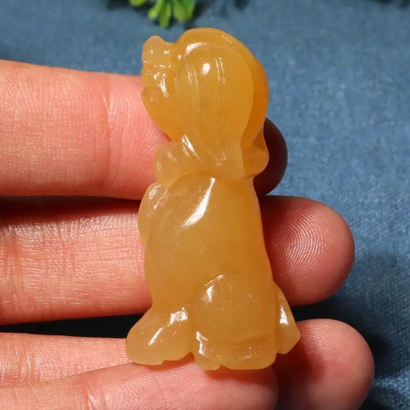 Yellow stone sculpture of a figure held between fingers against a blue background