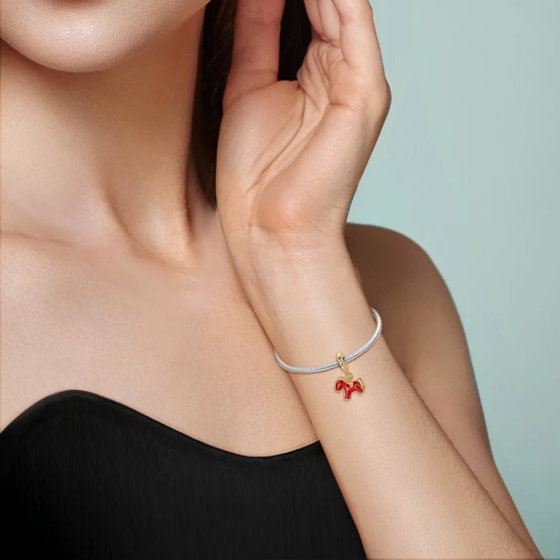Close-up of a person wearing a bracelet with a red dog charm on a light background