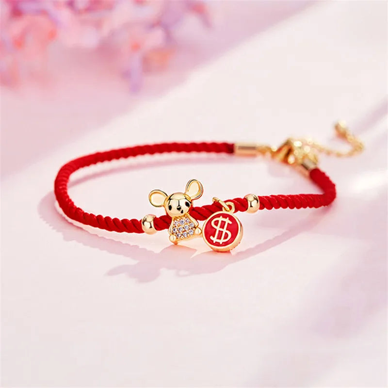 Red string bracelet with gold mouse charm and dollar sign on a pink background