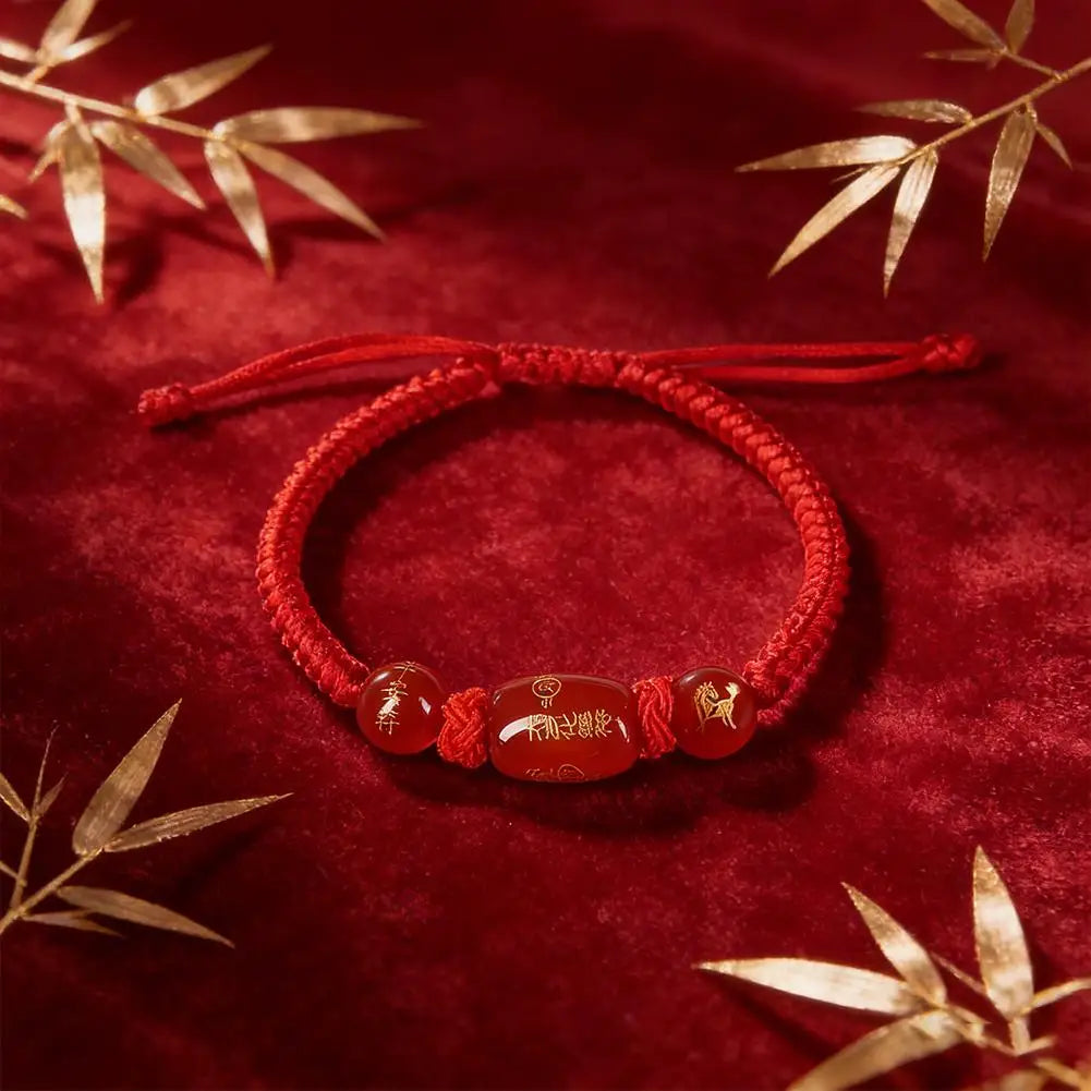 Red braided bracelet with three beads on a red background with gold leaves