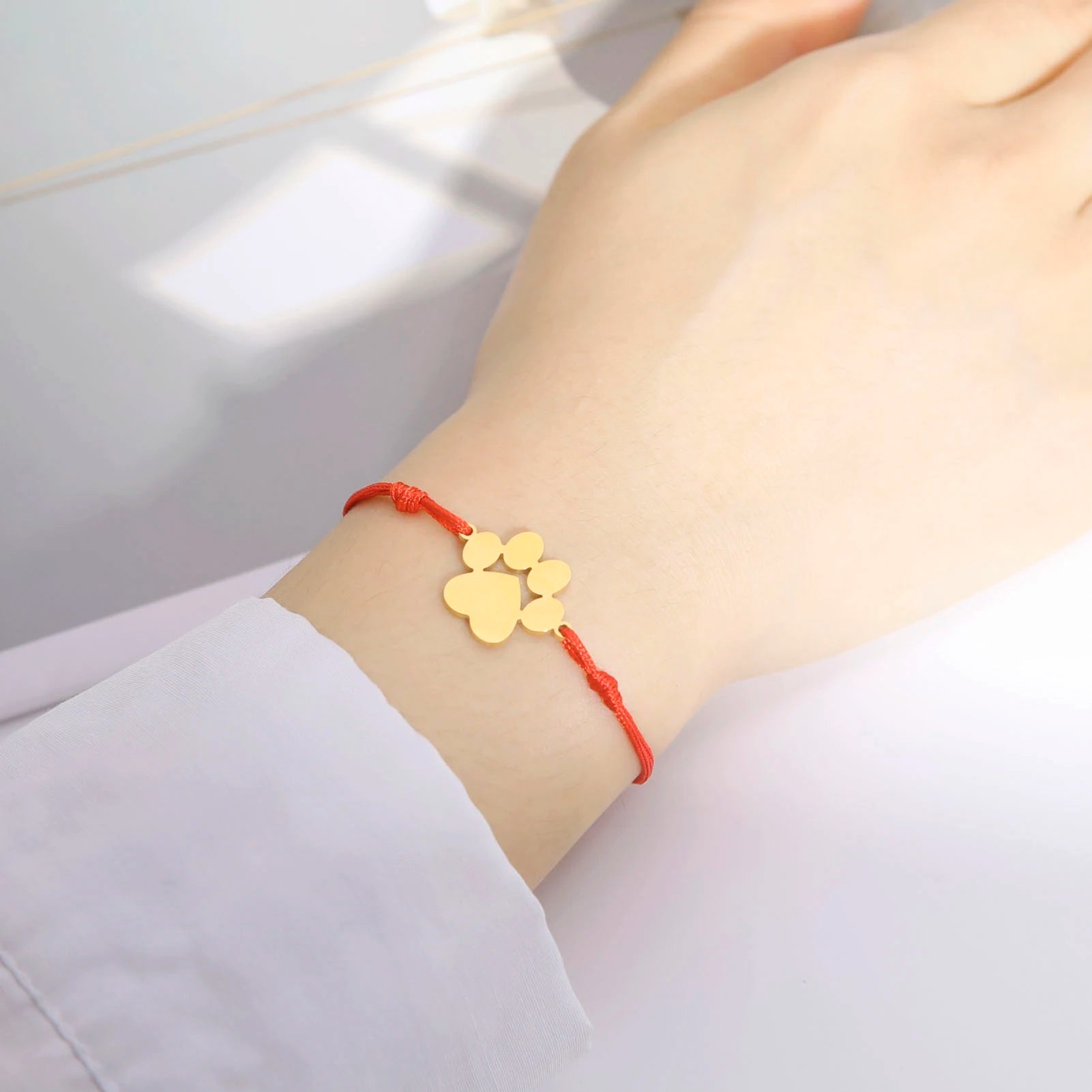 Gold paw print charm on a red string bracelet worn on a wrist with a light background