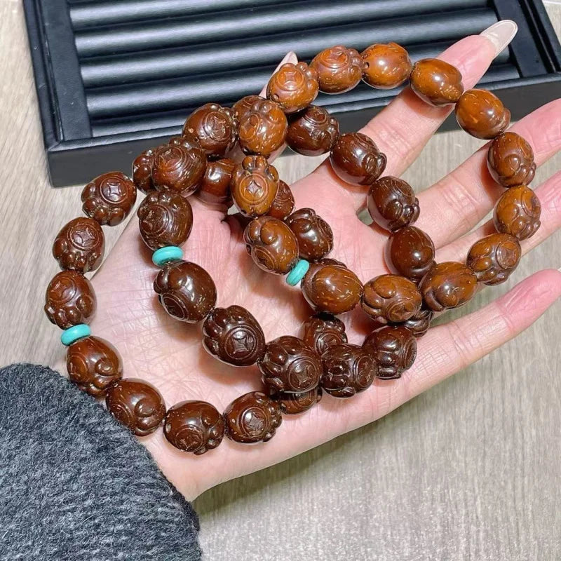 Hand holding a bracelet with brown beads and turquoise accents on a wooden surface.