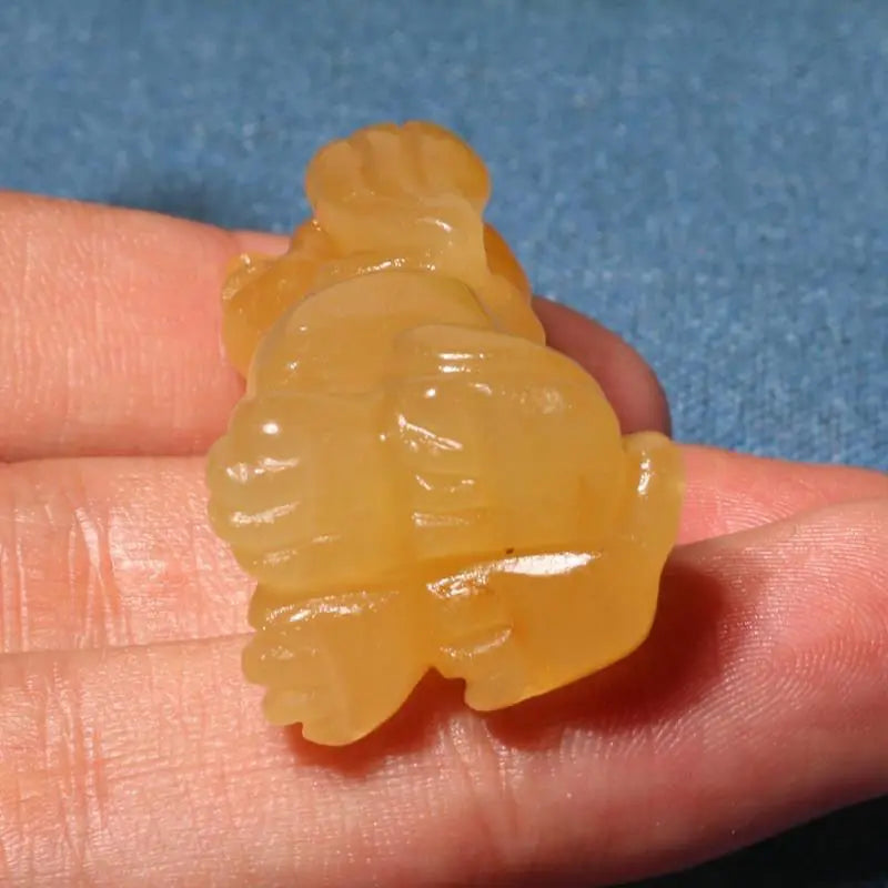 Yellow jade carving held in a hand against a blue background