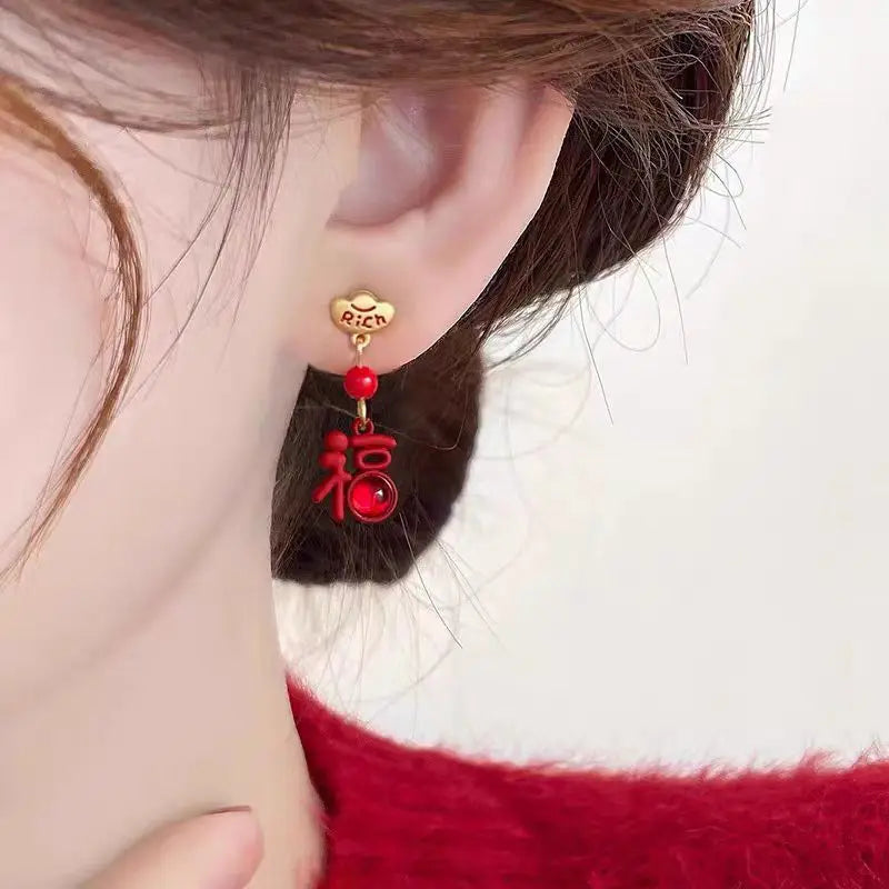 Close-up of an ear wearing a red and gold earring with Chinese characters on a white background.