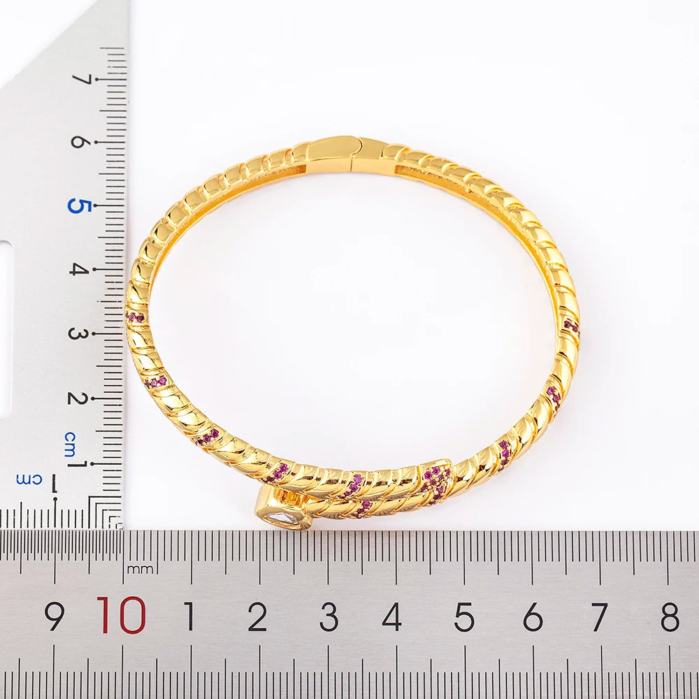 Gold bracelet with embedded stones on a white background with a ruler for scale.