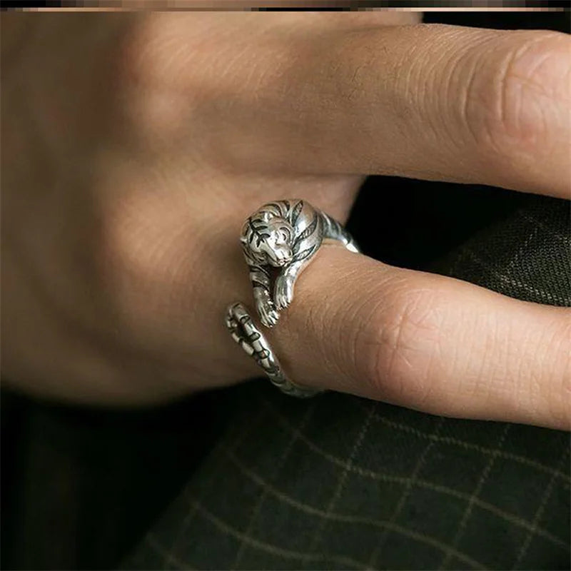 Silver ring with a tiger design on a finger against a dark background