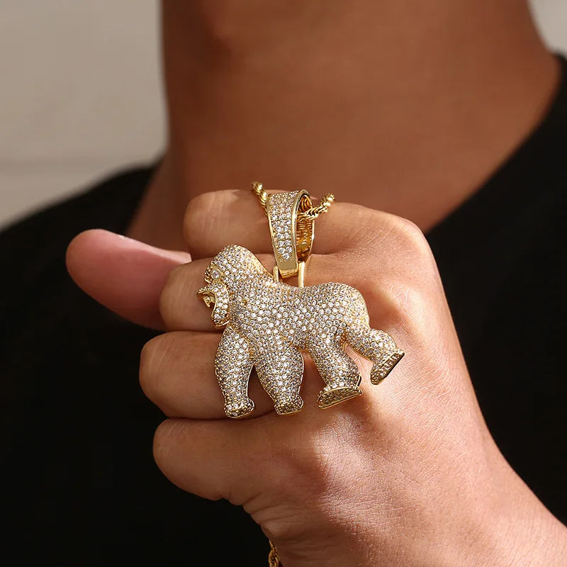 Gold gorilla pendant on a chain held in a hand against a neutral background