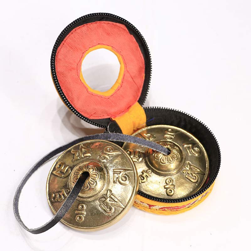 Pair of gold tingsha bells in a black and red case on a white background