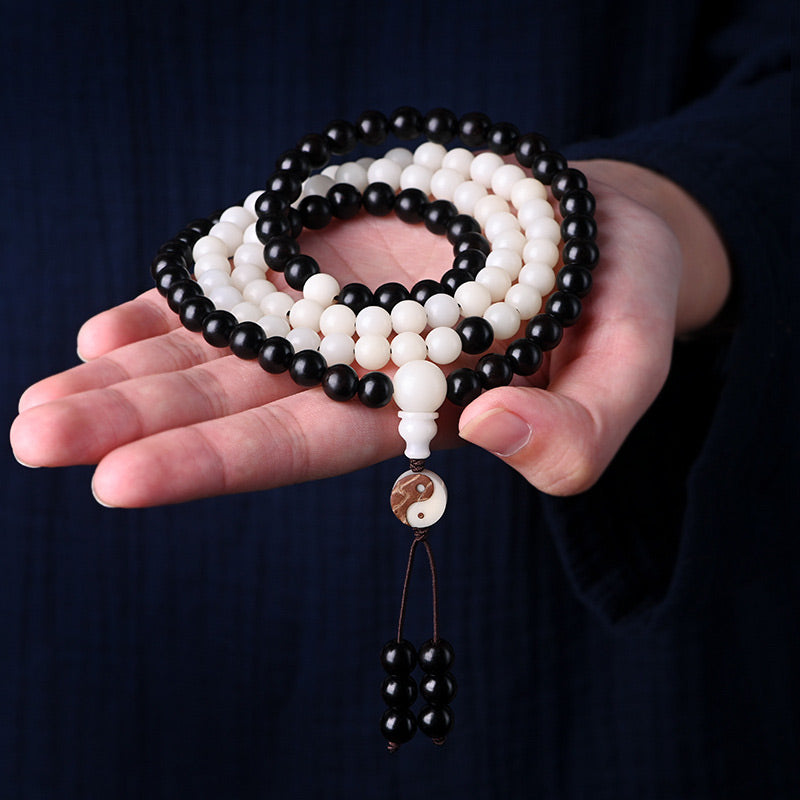 Black and white beaded necklace with a yin-yang pendant held in a hand against a dark background