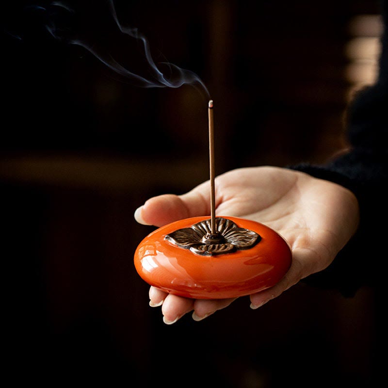 Hand holding an orange incense burner with a smoking stick inside, dark background