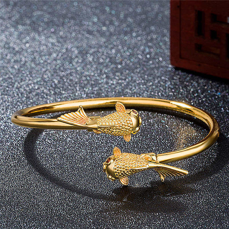 Gold bracelet with fish designs on a textured gray surface