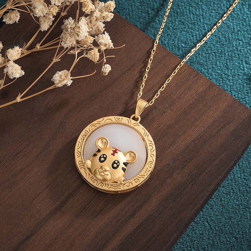 Gold pendant with a bear design on a wooden surface with dried flowers.