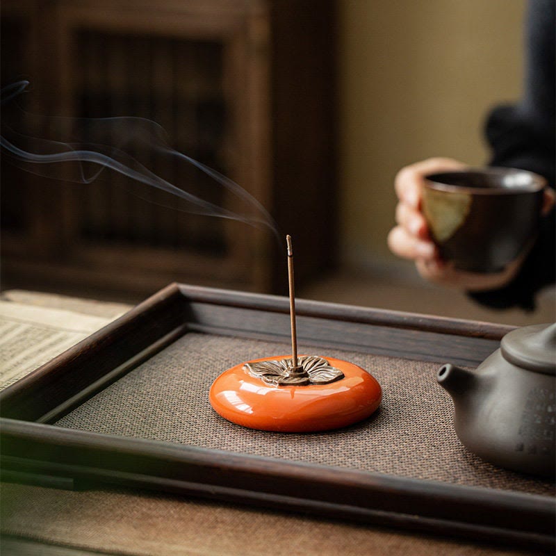 Incense burner with smoke on a tray, with a person holding a cup in the background