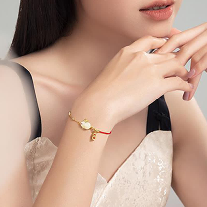 Woman wearing a gold bracelet with a red string on a neutral background