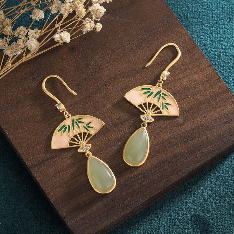 Gold earrings with green accents on a wooden surface
