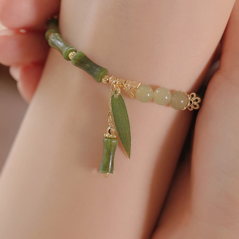 Green beaded bracelet with leaf charm on a wrist against a neutral background