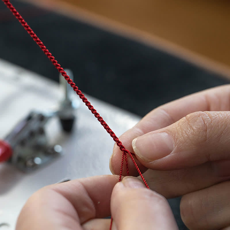 Close-up of hands threading red thread through a needle with sewing equipment in the background.