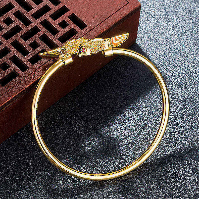 Gold bracelet with bird-shaped clasp on a dark textured surface
