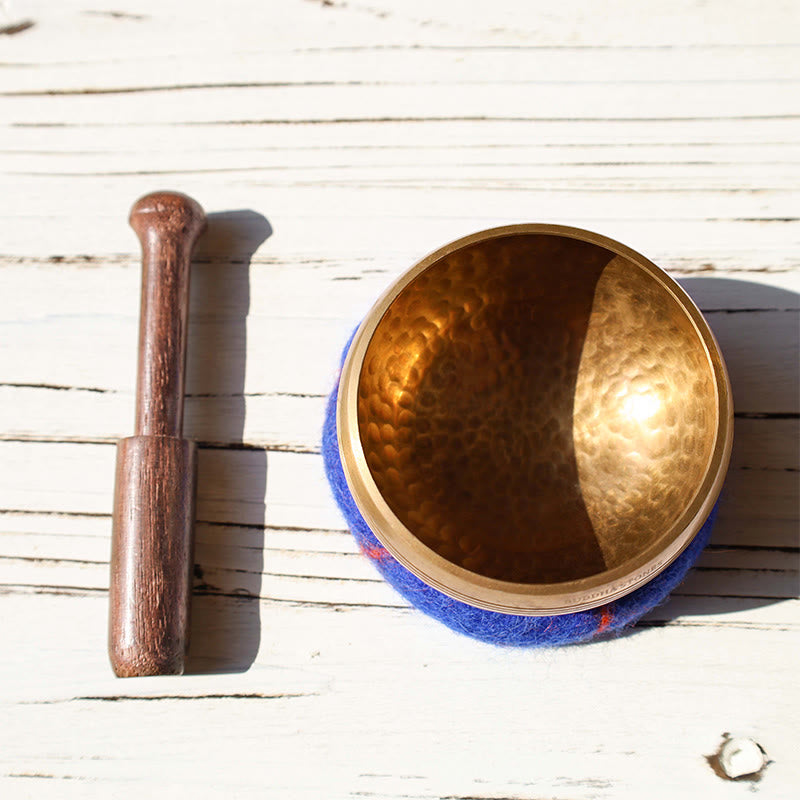 Bronze singing bowl with wooden striker on a wooden surface