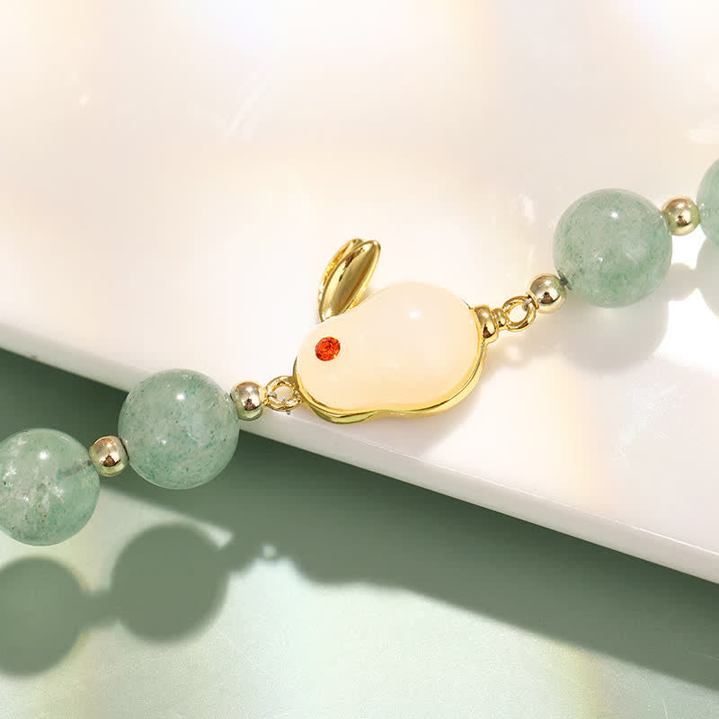 Bracelet with green beads and a gold charm on a white surface
