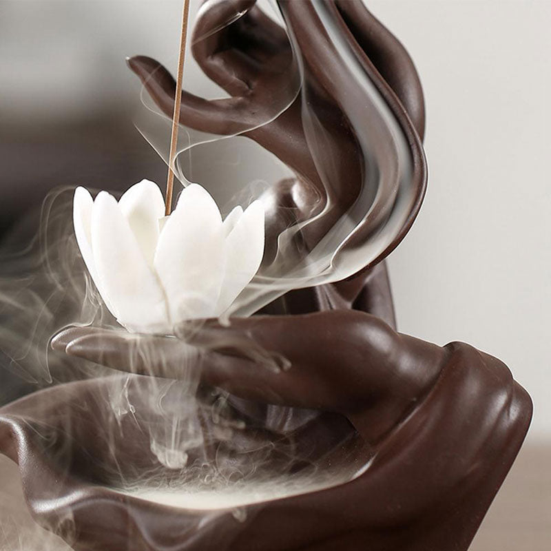 Ceramic incense burner with lotus design and incense sticks emitting smoke.