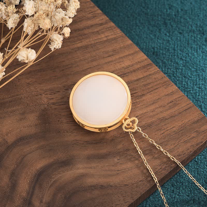 Gold necklace with a round pendant on a wooden surface with dried flowers.