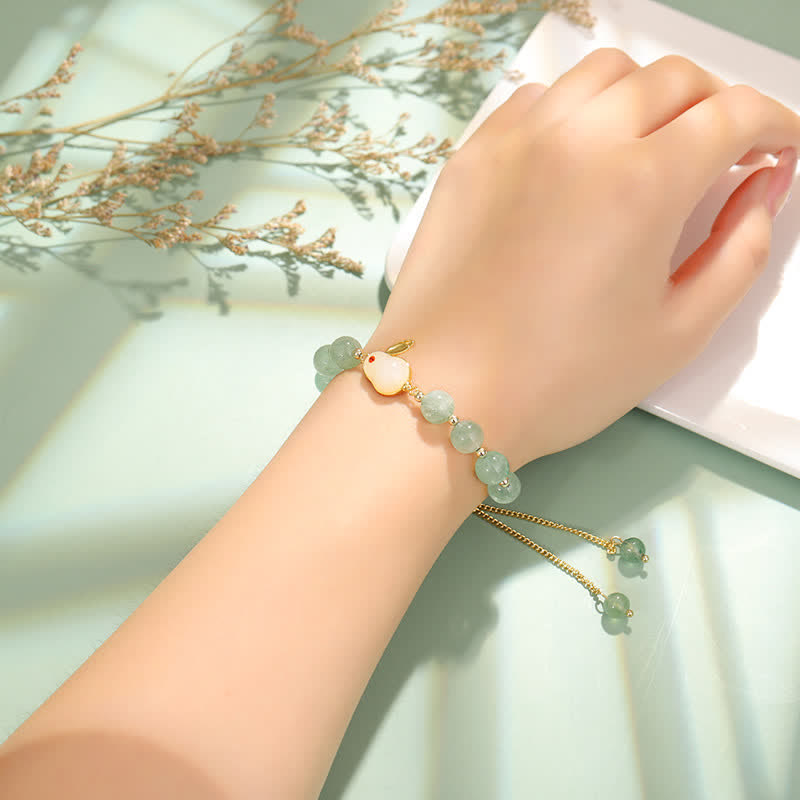 Hand wearing a bracelet with green beads and gold accents on a light background