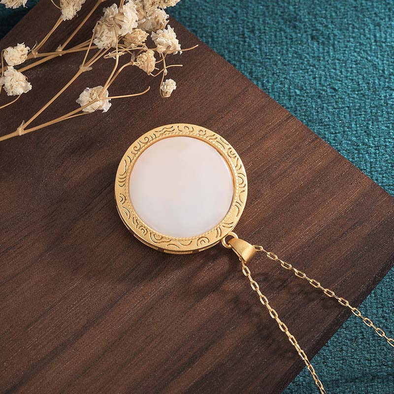Gold necklace with a round pendant on a wooden surface with dried flowers.