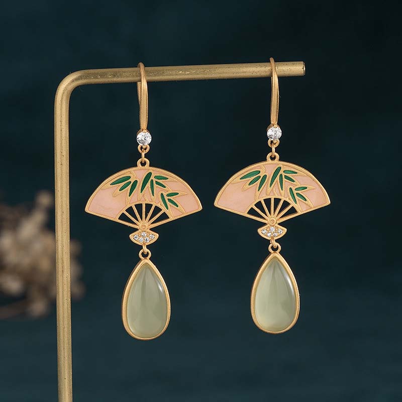 Gold earrings with green leaf design and teardrop-shaped stones on a dark background