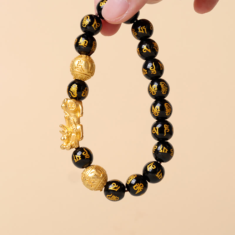 Hand holding black obsidian bracelet with golden PiXiu charm