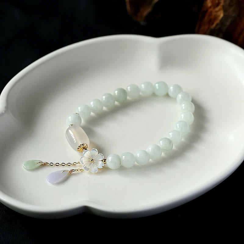 Serene Blossom White Jade Bead Bracelet by TheFuMaster, featuring natural white jade beads and blossom charm on a white dish.