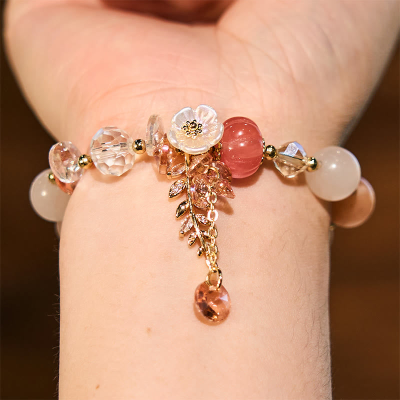 Delicate bracelet with floral and berry charms on a wrist against a neutral background