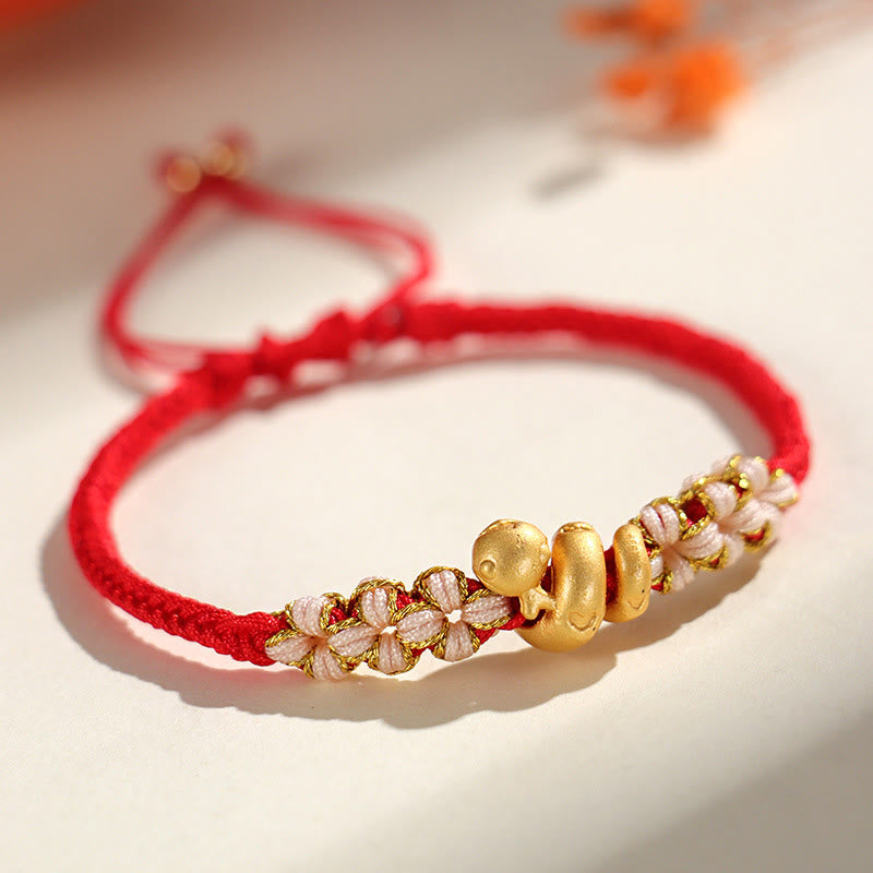 Gold bracelet with floral beads on a red string against a light background