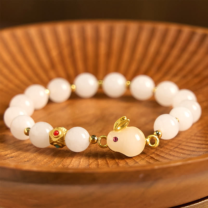 White beaded bracelet with gold accents and red stones on a wooden surface