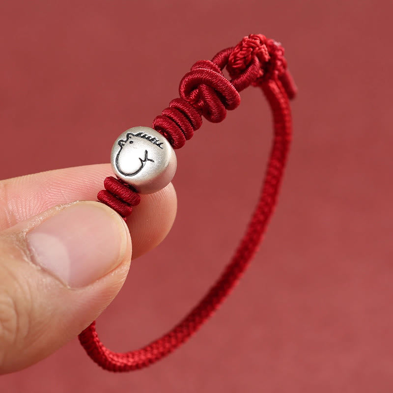 Red string bracelet with a silver charm held between fingers against a red background