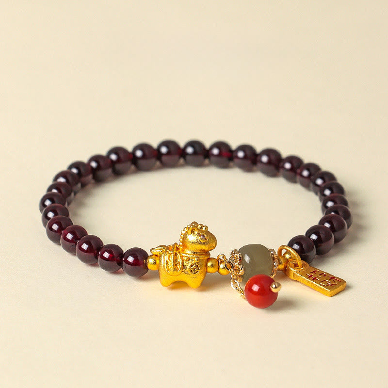 Garnet beaded bracelet with gold and red charm on a beige background