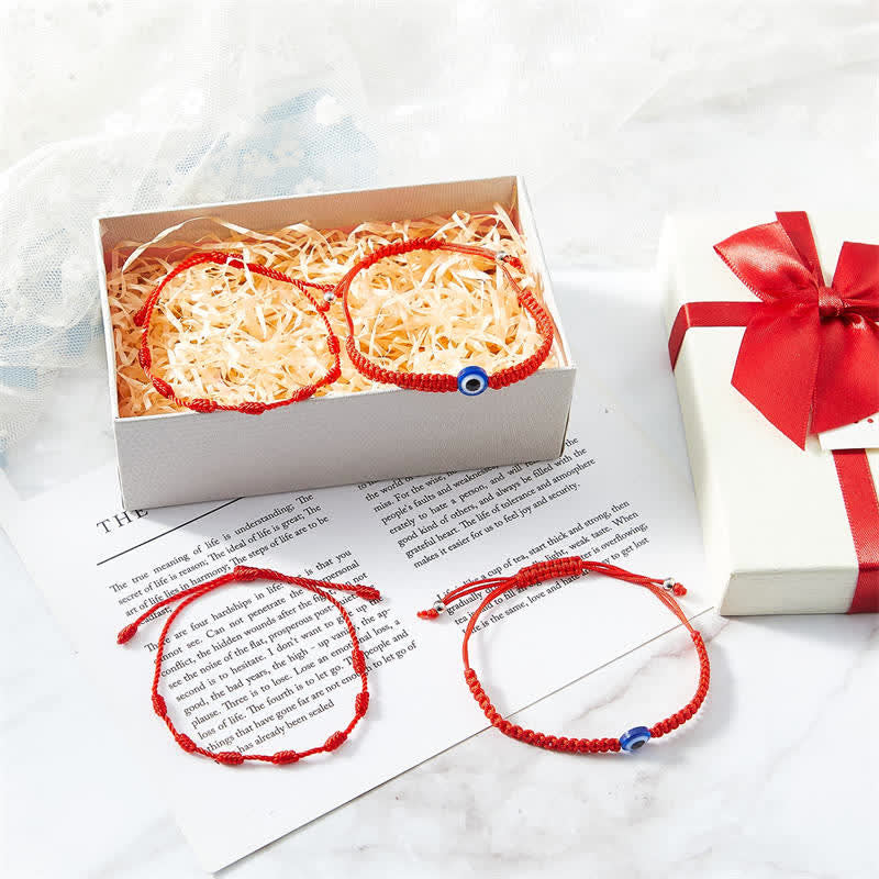 Red bracelets with blue beads on a white marble surface with a gift box.